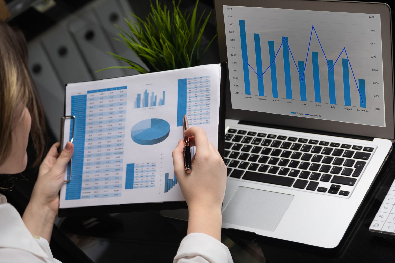 Analyst reviewing a business report on paper and a laptop