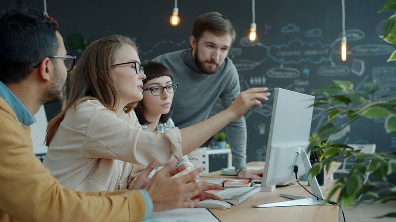 Colleagues in an office discussing work on a computer screen