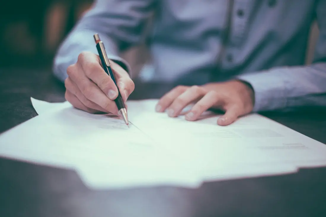 A person filling in paperwork with a pen at a desk