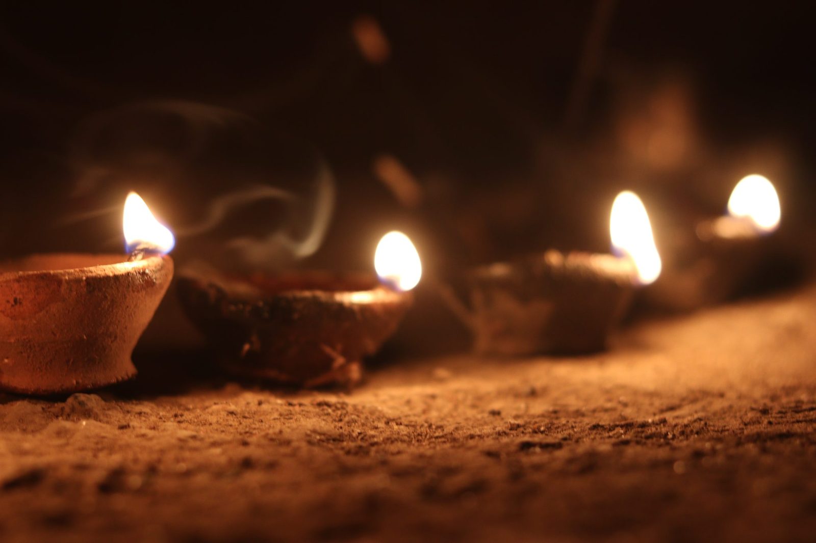 A row of lit clay diyas glowing on a dark floor during Diwali