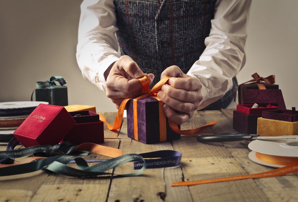 Hands tying a ribbon on a small gift box at a wooden workbench